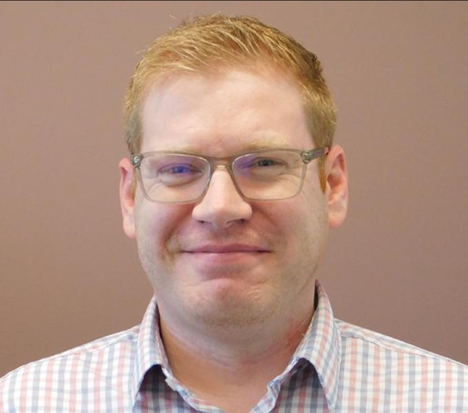 A picture of Sean Farris, a white man with short, red hair wearing clear-framed glasses